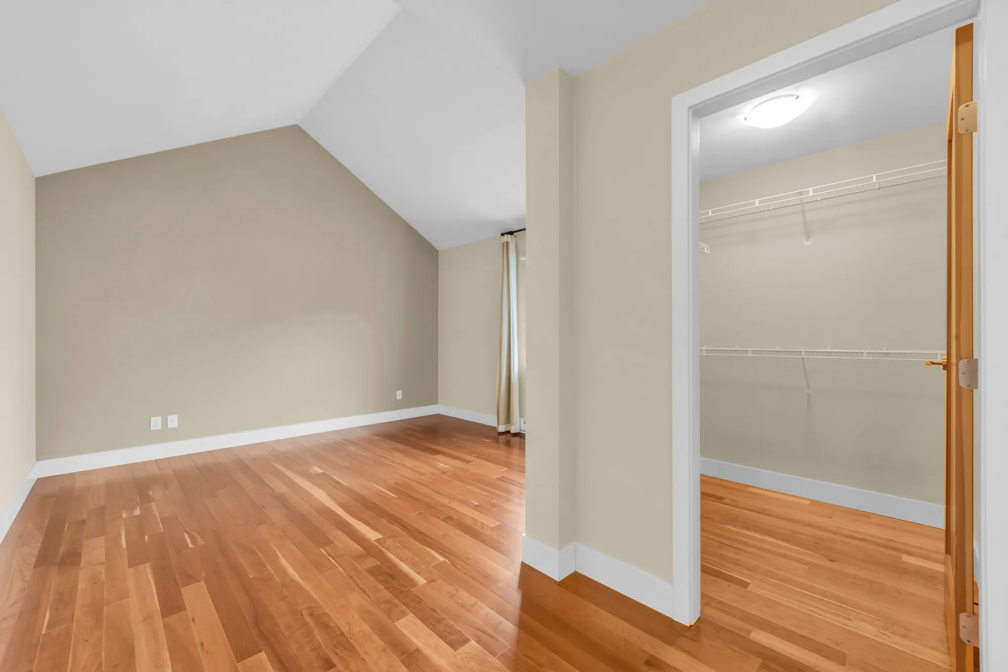 A walk-in closet with wire shelving, its door open, the bedroom at the left
