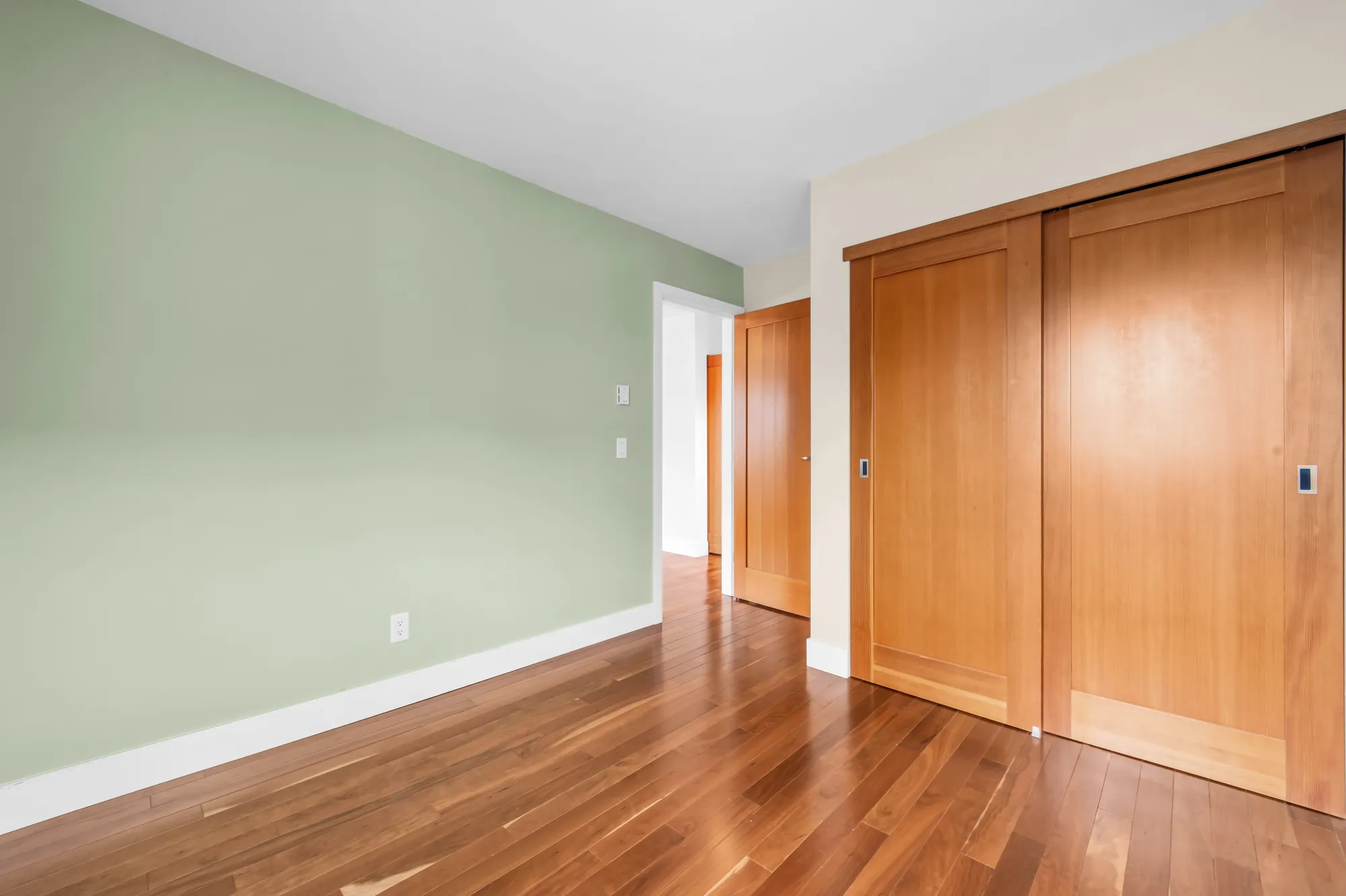 The third bedroom toward its double closet with wood sliding doors and the door to the hall, a sage green wall