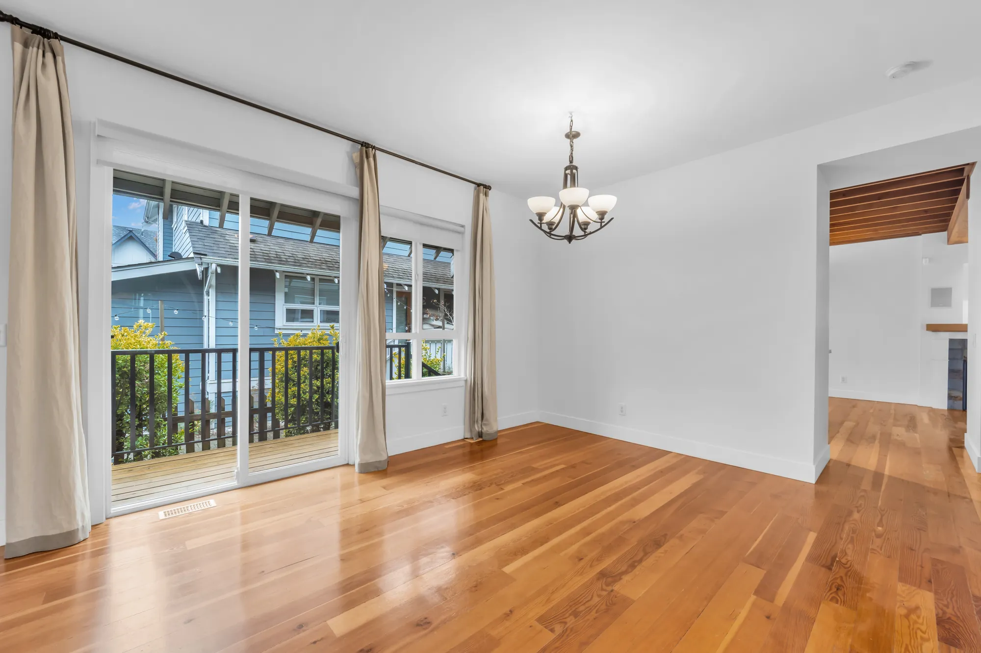 The dining room&rsquo;s sliding door and window onto the side deck, long curtains, a chandelier, the kitchen through a doorway at the right