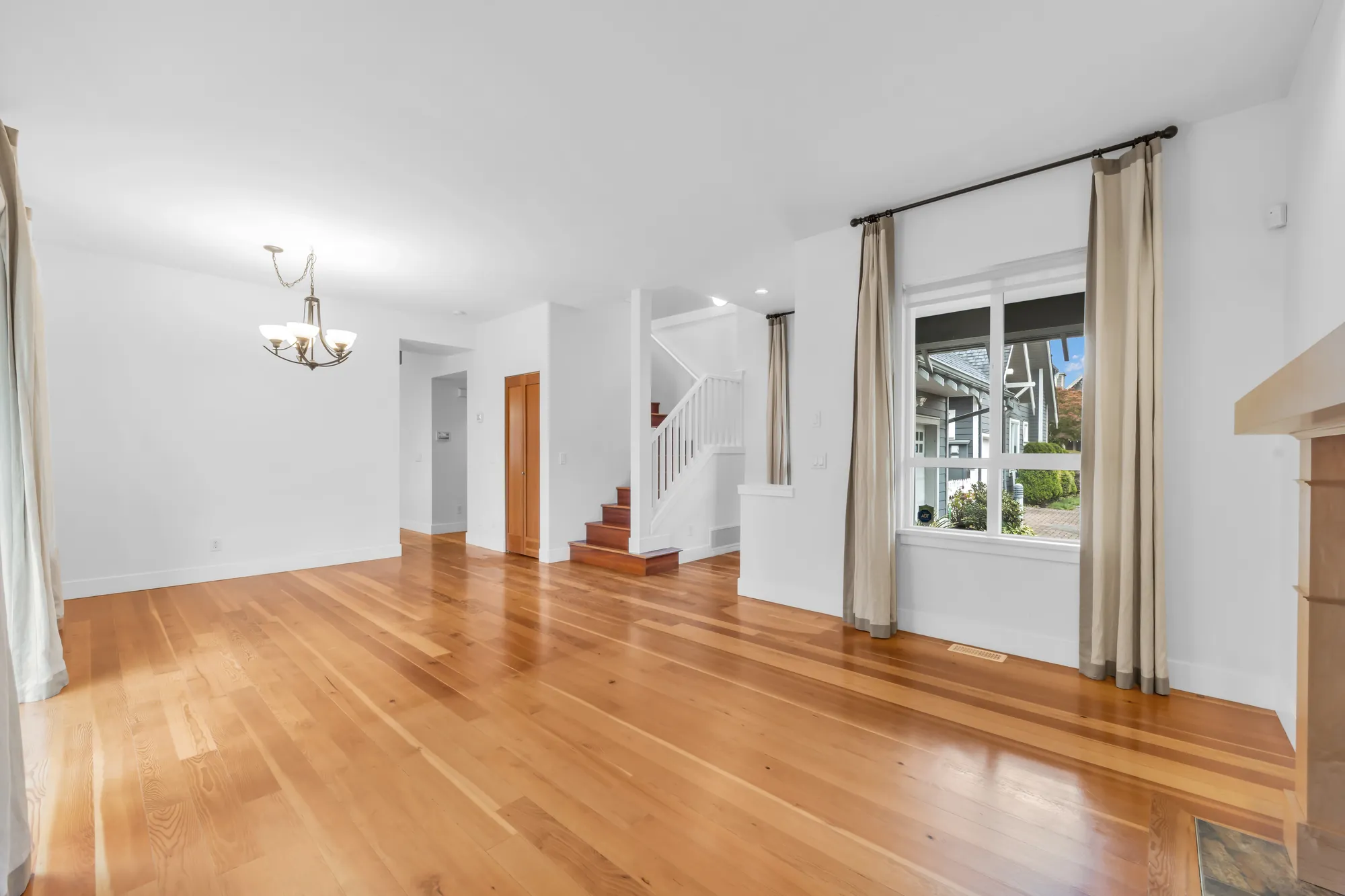 From the living room toward the dining room, the stair with a white railing and a front window with long curtains