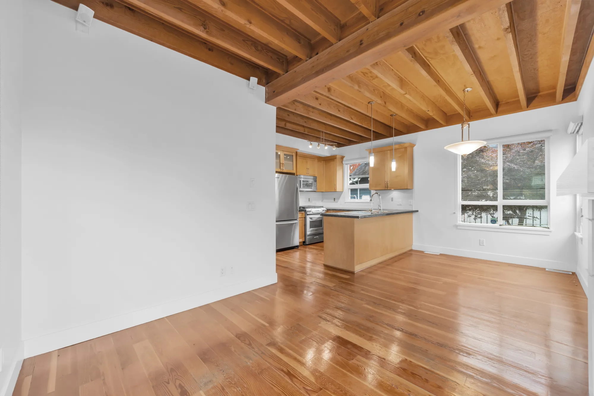 The eating area and the kitchen from the family room: a window with blinds, a bowl pendant light, the peninsula and the stainless appliances