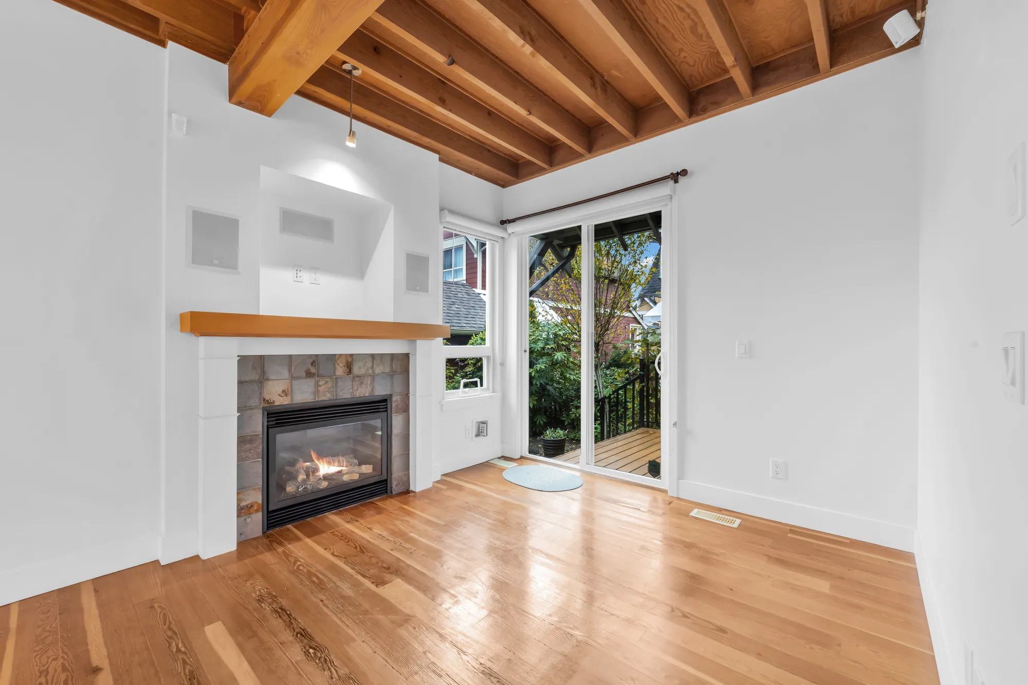 The family room&rsquo;s fireplace in slate tile with a wood mantel, the sliding door to the back deck, wood joists overhead