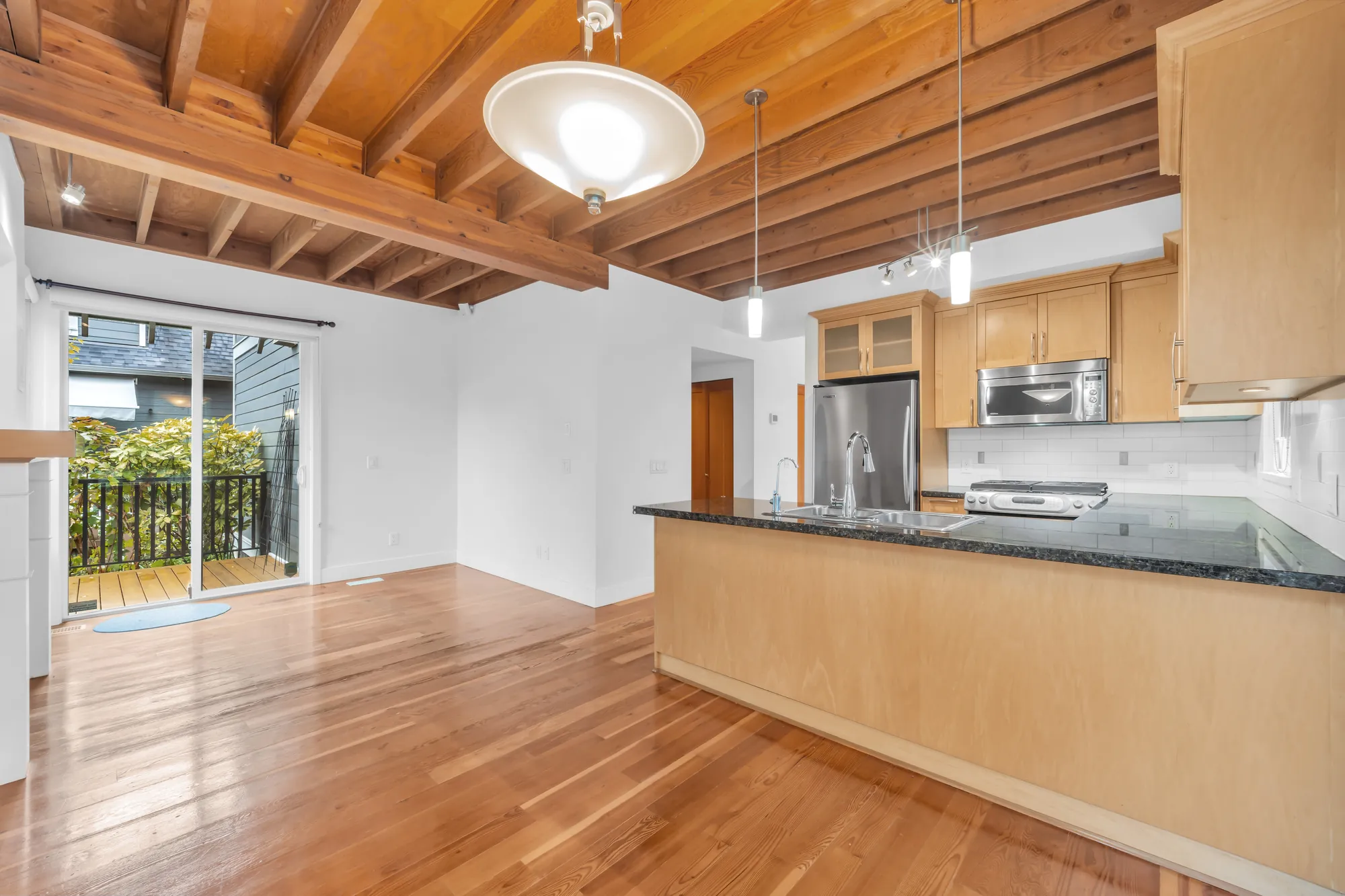 From the eating area toward the kitchen: the sliding door to the back deck at the left, the peninsula, the refrigerator, microwave and range, a bowl pendant light