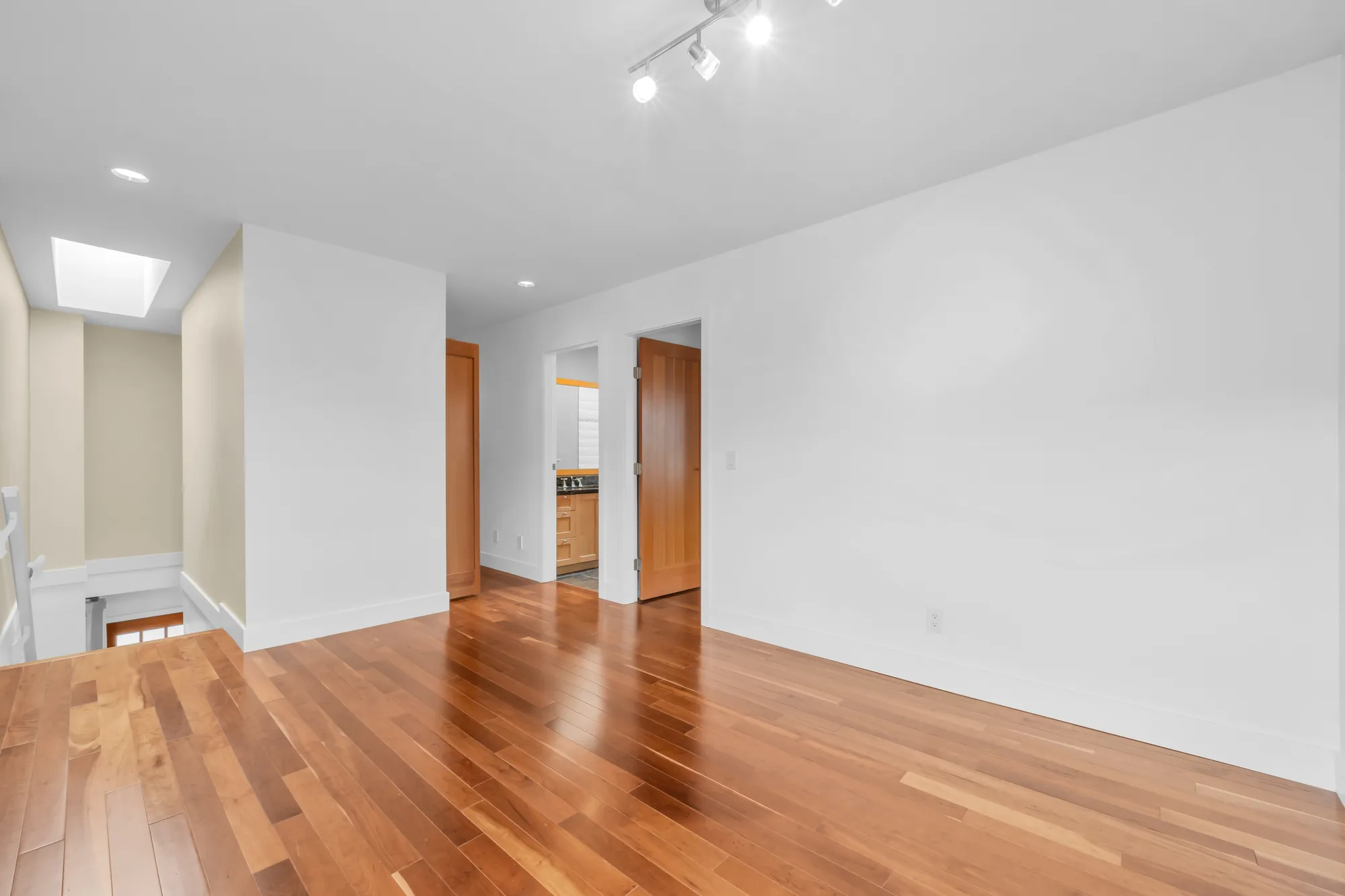 The flex room toward the stair and the hall: a skylight above the stair, wood doors along the hall, track lights