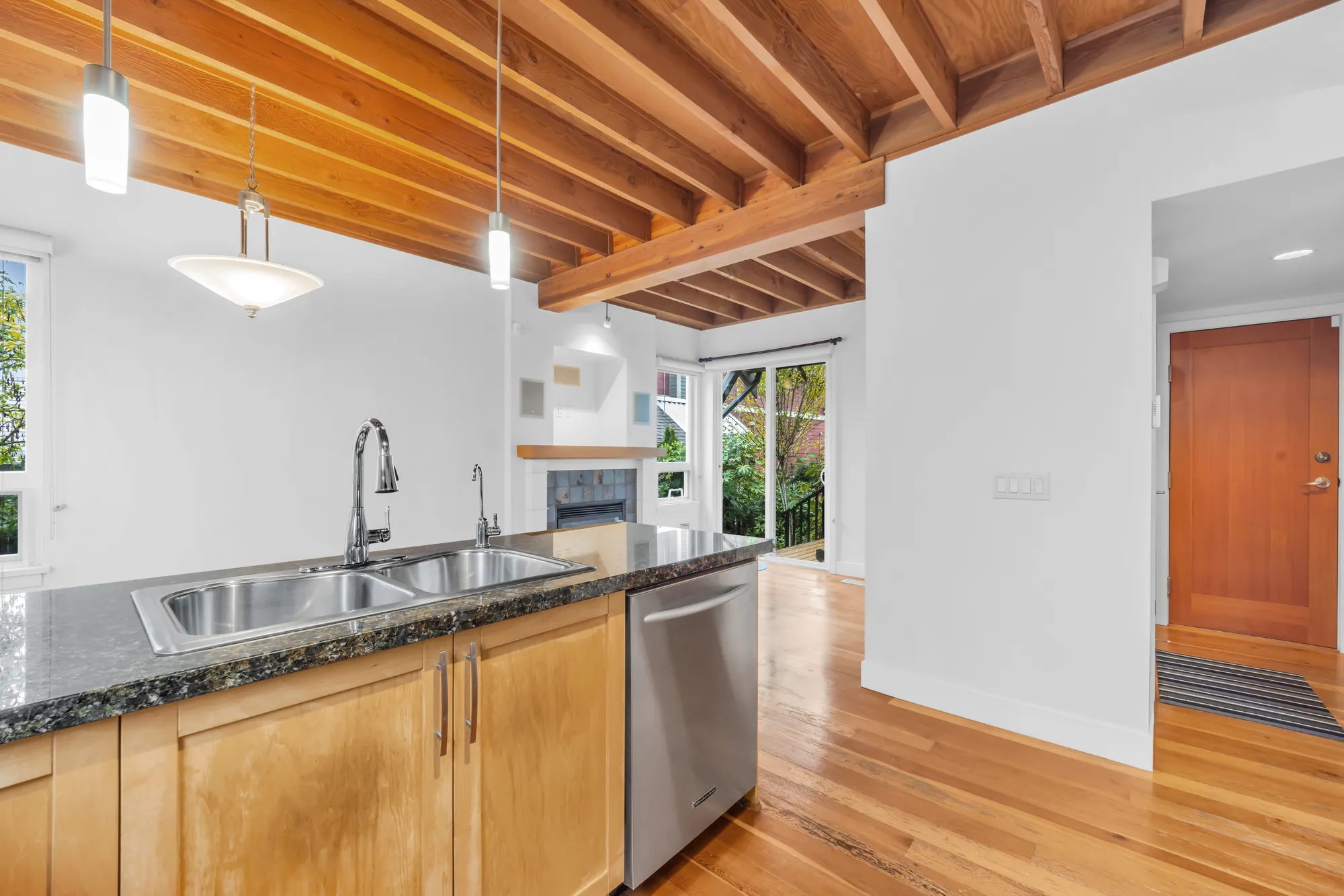 The sink in the peninsula and the dishwasher, the family room and its fireplace beyond, a wood door at the right