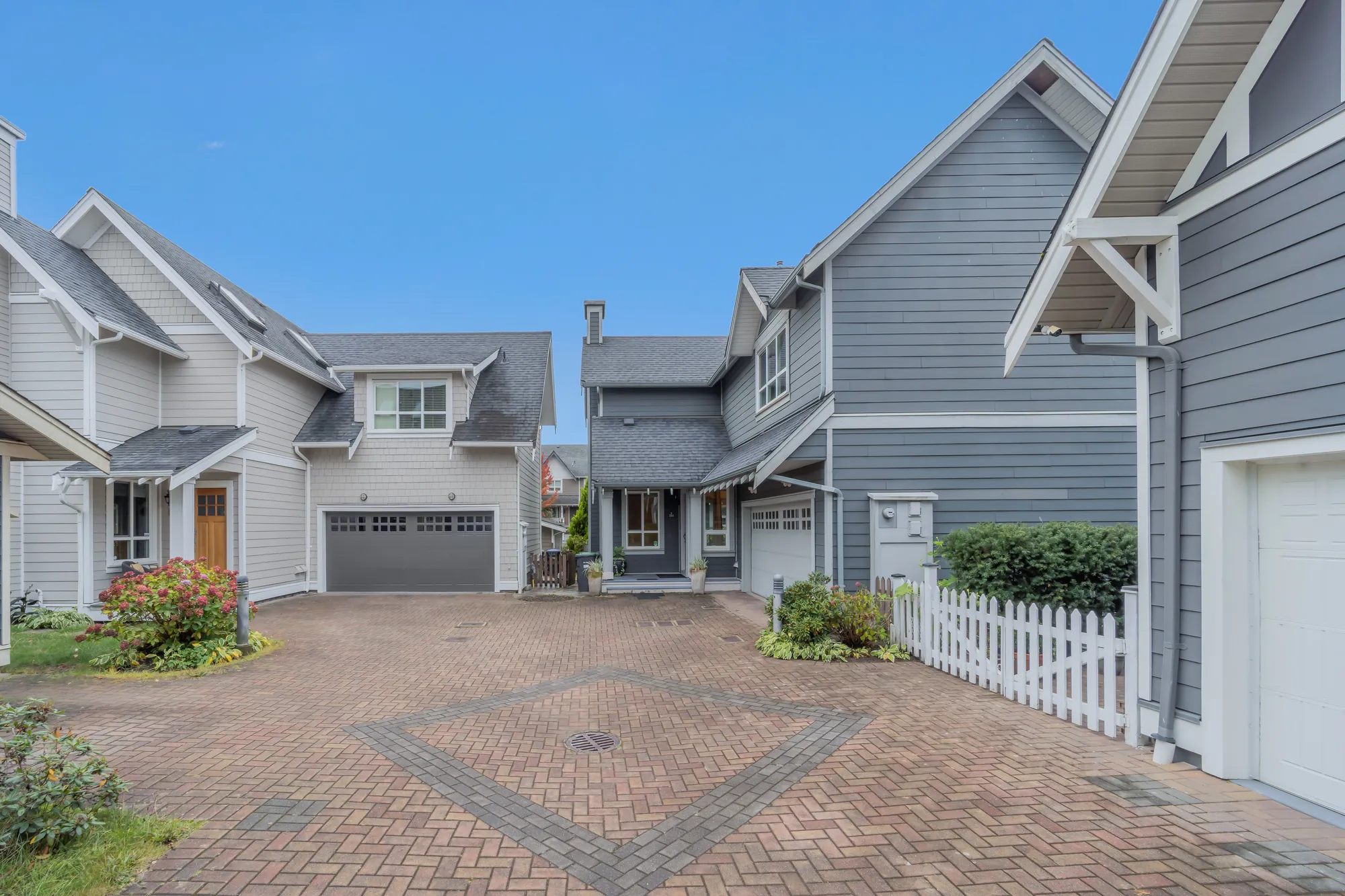 The brick-paved court with a diamond pattern laid in it, two-storey houses with porches and garages around it, the white picket fence at the right