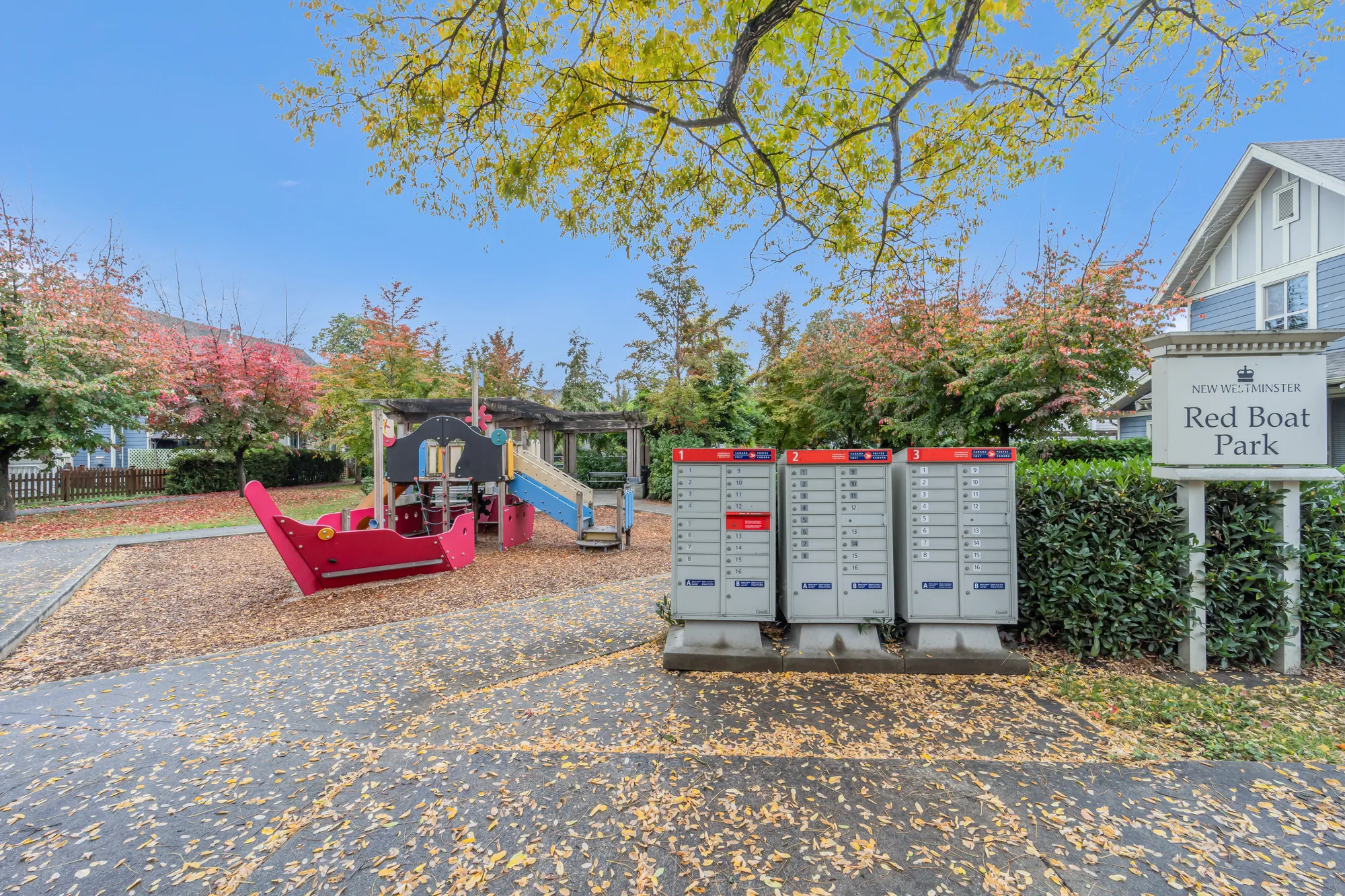 Red Boat Park: a playground with a red boat and a slide on wood chips, a bank of mailboxes, a sign reading Red Boat Park, trees in autumn colour