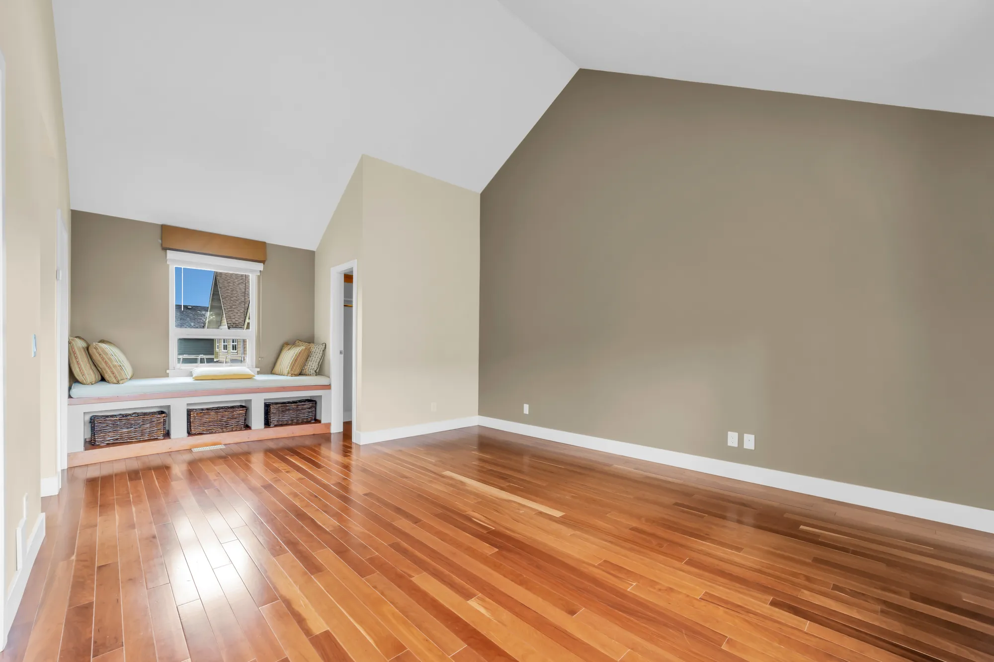 The primary bedroom toward the window seat at the far end, the vaulted ceiling, a tall taupe wall at the right